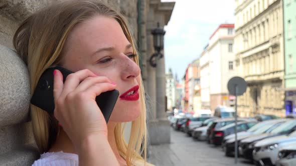 A Young Beautiful Woman Leans Against a Wall in an Urban Area and Talks on Smartphone - Face Closeup