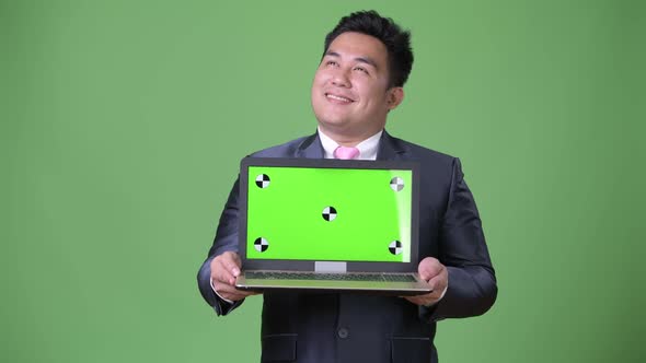 Young Handsome Overweight Asian Businessman Against Green Background