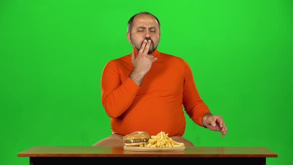 Man with Overweight Looks at Delicious Junk Foods on the Table Then Playing with French Fries, Green