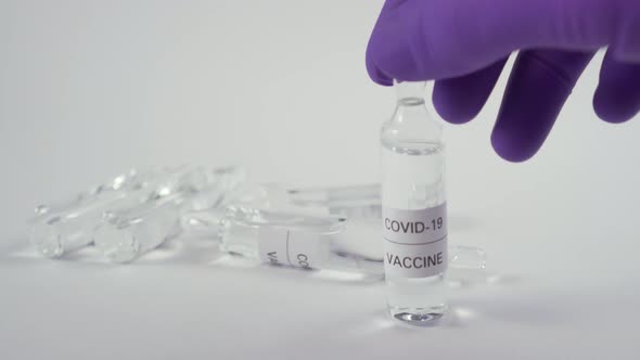 A hand in blue protective gloves puts the ampoule with the medicine for COVID-19 