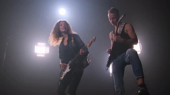 Two Rock Stars on Stage. A Lot of Light on Background. Guy in Black T-shirt Plays the Electric