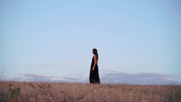 Side View of a Beautiful Brunette Model in Long Black Dress Going Towards the Sun