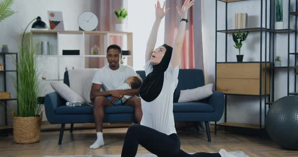 Woman in Headscarf Doing Stretching Exercises on the Floor near Her Black-Skinned Husband