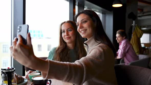 Two Young Attractive Girls in a Cafe Take Selfies Smile and Pose