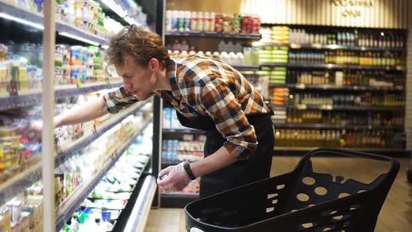 Salesman is Putting Cheese Packs From the Cart on Shelves in Milk Products Department in Food Store