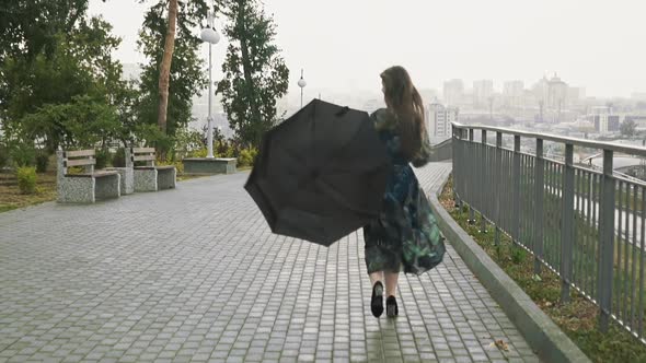 Happy Woman in Stylish Dress with Umbrella Runs Along Park