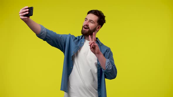 A Man Taking a Selfie on His Phone Posing and Making a Victory Gesture