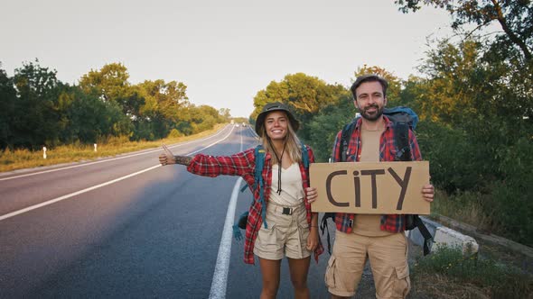 Couple of Travelers Hitchhiking on Road with Sign City