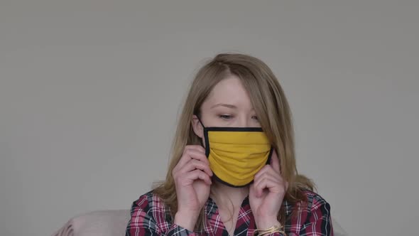 Young Caucasian Woman Putting on Yellow Face Mask and Headphones and Waving Hello at Camera