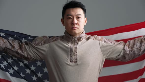 Serious soldier Asian man covered with the USA flag looking at the camera