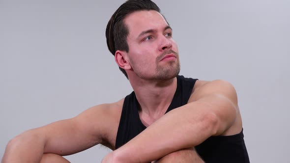 A Young Handsome Man in a Tanktop Sits and Looks Around - Closeup - White Background