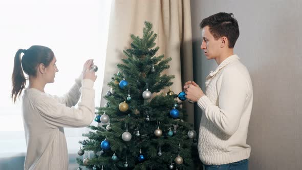 Handsome Young Man and Pretty Lady Decorate Christmas Tree