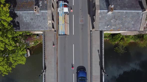 Top down of an old stone bridge with toll buildings incorporated, traffic filtering through with roa