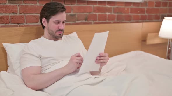 Young Businessman Reading Documents in Bed