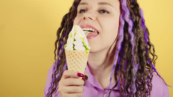 Young woman licking ice cream on yellow background.