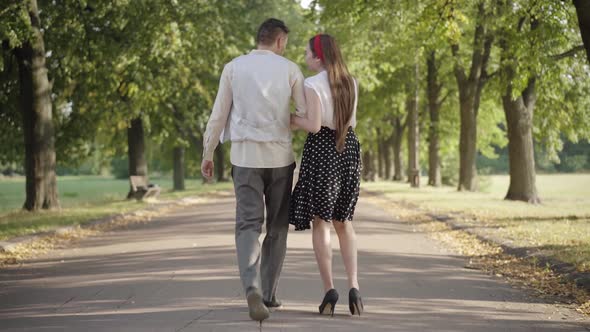 Wide Shot of Young Couple Dating in Sunny Summer Park. Back View of Slim Young Woman and Elegant Man