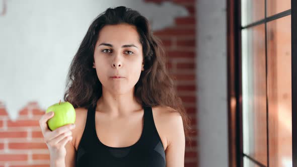 Portrait of Hispanic Smiling Fitness Young Girl Eating Fresh Green Apple Looking at Camera