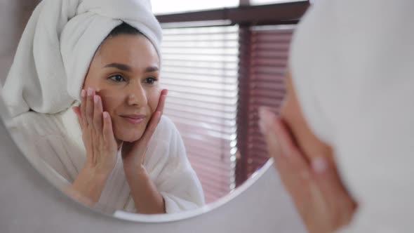 Young Hispanic Woman with Towel on Head After Shower Looks in Mirror Washes Face Healthy Soft Clean