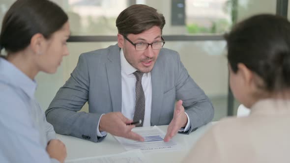 Middle Aged Businessman with Papers Scolding Female Colleagues