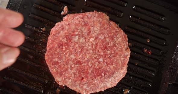 A Man's Hand Puts a Raw Burger in the Pan. 