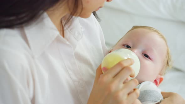 Caucasian beautiful mother holding and feeding baby from milk bottle in bedroom