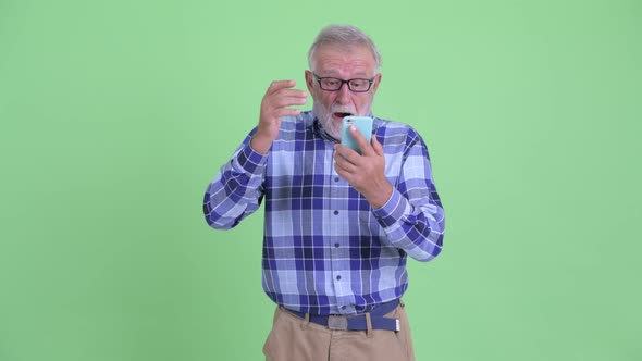 Happy Senior Bearded Hipster Man Using Phone and Looking Surprised