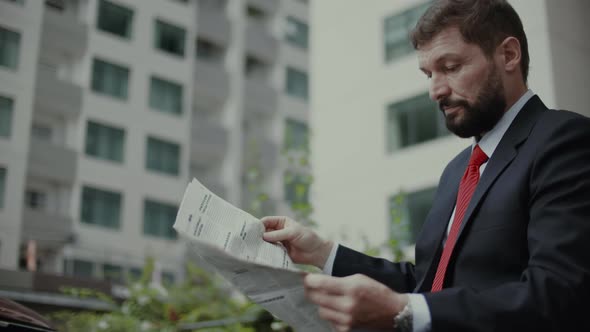 Businessman Senior in an Expensive Suit with a Beautiful Beard in Black Blue Jacket Sits on Bench in