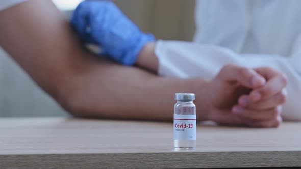 Closeup of Bottle of Covid19 Vaccine with Medicine Against Coronavirus Stands on Wooden Table in