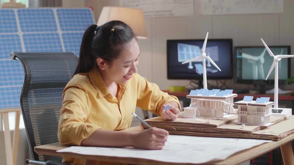 Asian Woman Sketch House With Solar Panel On The Blueprint While Holding It In Hand