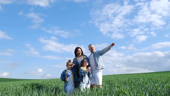 Cheerful Family Walks Through a Green Field of Wheat