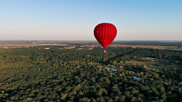 A beautiful red balloon flies in the evening over the river and the city.