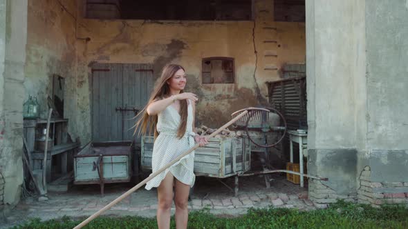 Barefoot Woman Holds Rake Walking on Grass Against Building