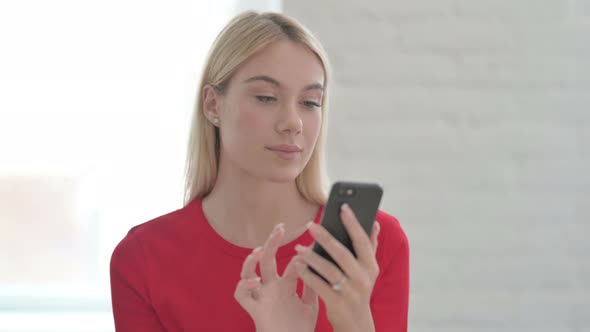 Young Blonde Woman Celebrating Online Success on Smartphone