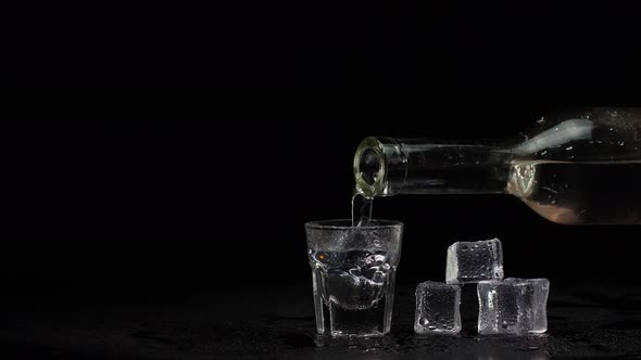 Barman Hand Pours Vodka Tequila or Sake From Bottle Into Glass on Black Background with Ice Cubes