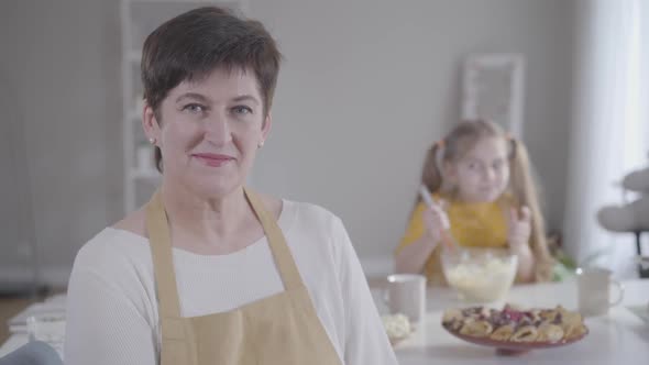 Close-up Portrait of Happy Caucasian Adult Woman Smiling at Camera As Blurred Little Girl Licking