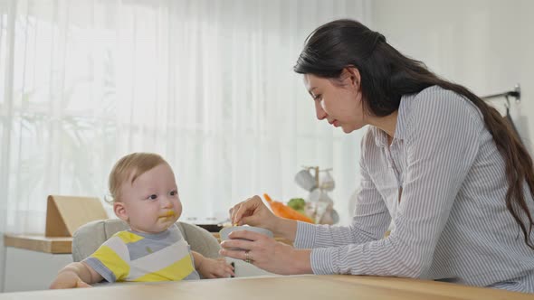 Caucasian attractive parents mother feeding healthy foods to baby boy toddler in kitchen at home.