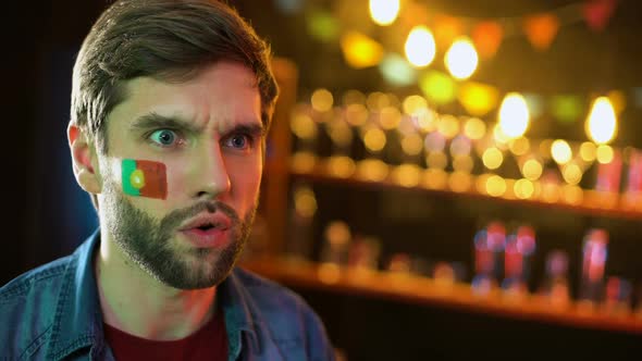 Nervous Portuguese Football Fan With Flag on Cheek Making Facepalm, Team Losing