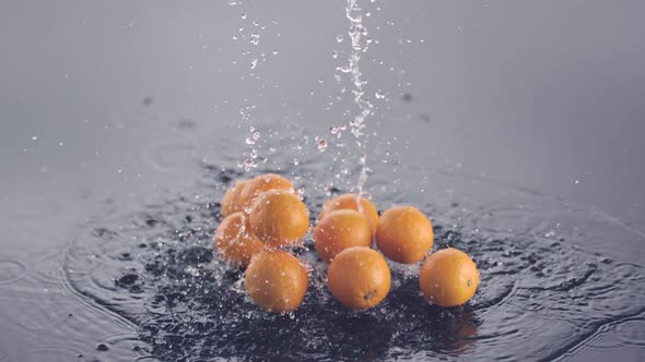 Fresh oranges and water fall down onto a surface in slow motion