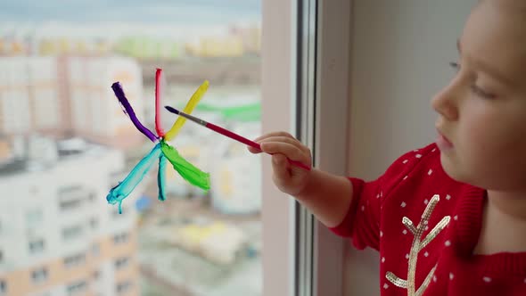 Child draw snowflake in rainbow colours on window with paints. Caucasian female person decorate room