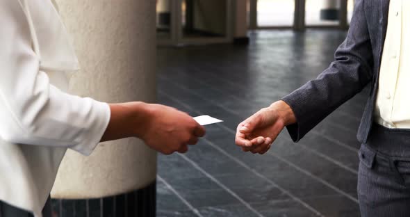 Mid section of executives shaking hands and giving visiting card