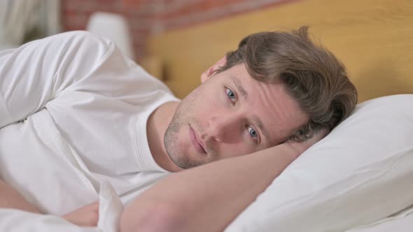 Portrait of Tired Young Man Looking at Camera From Bed