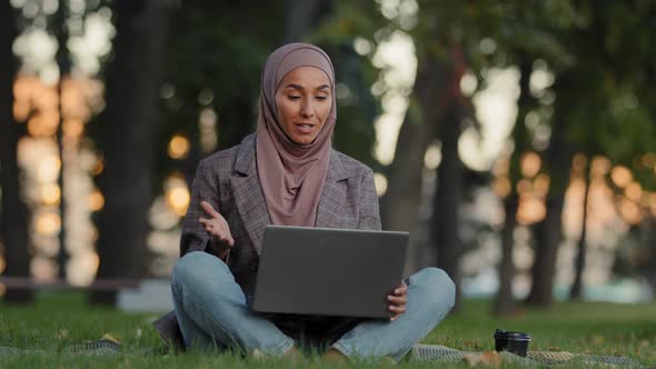 Happy Smiling Friendly Islamic Woman Muslim Girl in Hijab Sitting on Grass Lawn in Park Outdoors in