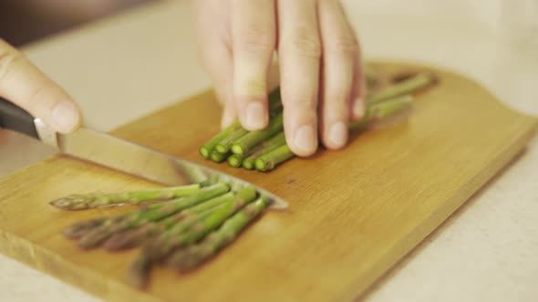 Chopping Raw Green Asparagus Before Cooking on a Wooden Board