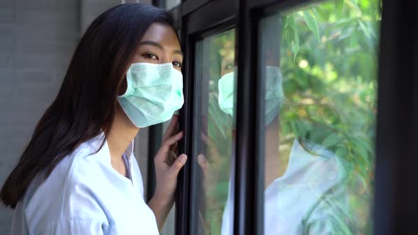 Sick Woman of Coronavirus Quarantine Looking Through the Window and Wearing a Mask for Protection