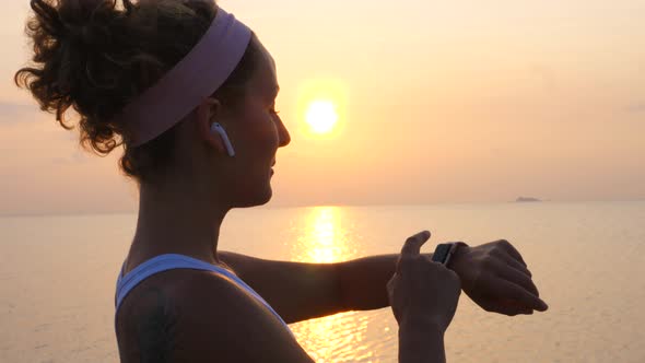 Active Sport Woman In Wireless Earphones Using Smartwatch At Sunset On Beach