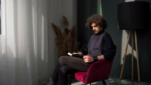 Man Sitting Near Window and Reading a Book on Background of Sunset