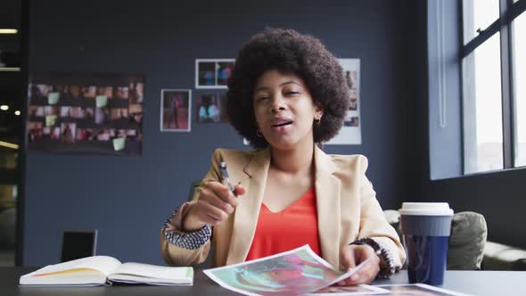 Mixed race businesswoman sitting having a video chat going through paperwork in a modern office