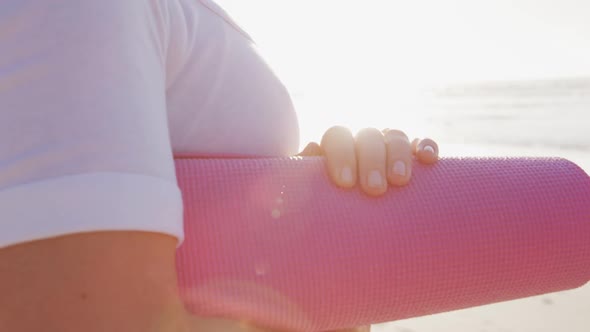 Caucasian woman holding pink sport mat on the beach and blue sky background