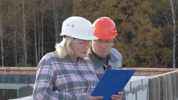 Funny Builders In Helmets Look At The Plan Then Wonder And Shake Their Heads