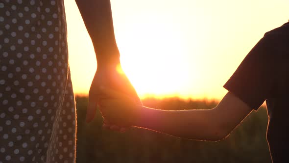 A Little Boy Takes His Mother's Hand in the Background of the Sunset. The Sun's Rays Pass Through